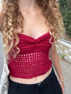 a woman with long curly hair wearing a red crochet top