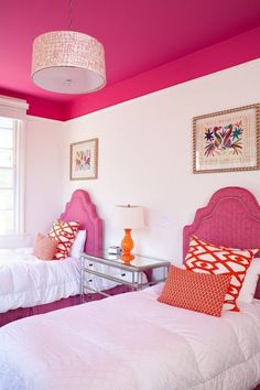 two beds in a room with pink walls and white bedding, one has orange pillows on it