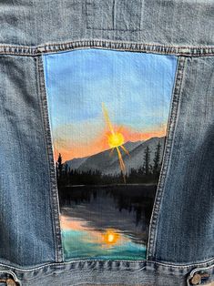 a painted jean jacket with the sun setting in the background and mountains on it's back