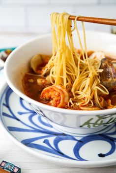 a bowl of noodles with shrimp and clams is on a blue and white plate