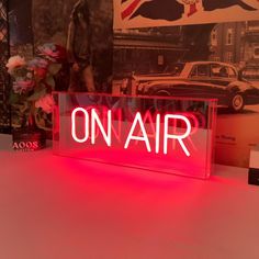 a neon sign that says on air in front of a wall with cars and flowers