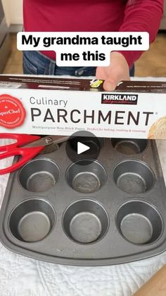 a person holding a box of muffins in front of an empty cupcake pan