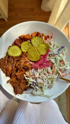 a white bowl filled with meat, coleslaw and pickles