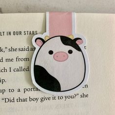 a bookmark with a cow on it's face in front of an open book