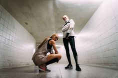 two young women are standing in an empty room and one is leaning on the floor