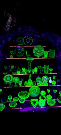 green glassware is lit up in the dark with neon lights around them and on shelves