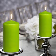 two lime green candles sitting on top of a table next to silverware and flowers