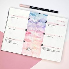 an open planner with pink, blue and purple watercolors on the pages next to a pencil