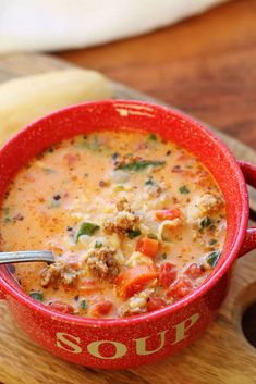 a red bowl filled with soup sitting on top of a wooden cutting board