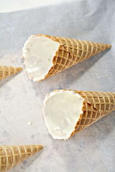 three ice cream cones with white icing in them on a piece of parchment paper