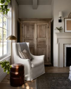 a living room with a chair, fireplace and armoire in the corner next to a window