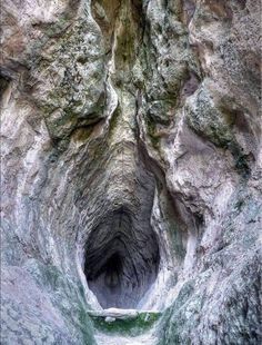 a narrow tunnel in the side of a mountain with moss growing on it's sides