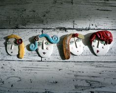 three ceramic masks hanging on the wall with different colored hair styles and colors, one is wearing