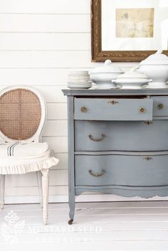 an old dresser is painted blue with white trim and gold hardware on the top, next to a wicker chair