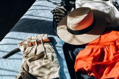 an open suitcase with clothes and hat on it sitting on top of a blue blanket