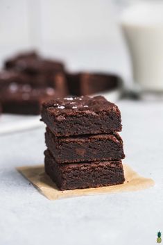 chocolate brownies stacked on top of each other in front of a white plate with one piece cut out