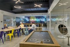 people are sitting at tables in an office with a pool table and neon signs on the wall