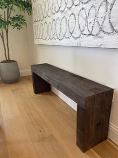 a wooden bench sitting next to a potted plant on top of a hard wood floor