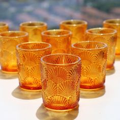 many yellow glass cups are lined up on a white tablecloth with the sun shining through them