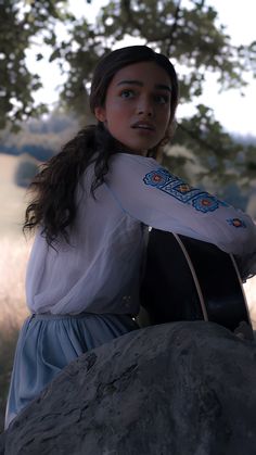 a woman in a dress sitting on top of a rock