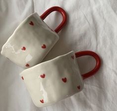 two red handled mugs with hearts painted on them sitting on a white cloth covered bed