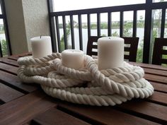 some white candles sitting on top of a wooden table next to a rope wrapped candle holder