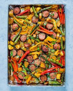 sausages, asparagus and peppers in a baking pan on a blue background