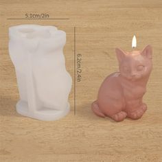 a small pink cat sitting next to a white candle holder on a wooden table with measurements