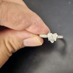 a woman's hand holding an engagement ring with a diamond in the middle, on top of a table