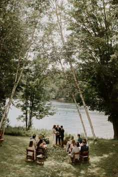 a group of people sitting on top of a lush green field next to a lake