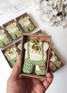 a hand holding a tiny crocheted green and white baby outfit in a box