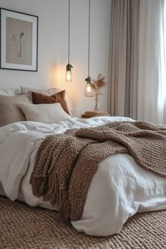 a bed with white linens and blankets on top of it, next to two hanging lights