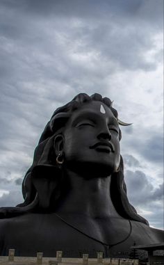 a large statue that is in the middle of a field with cloudy skies behind it