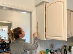 a woman is painting the cabinets in her kitchen with white paint and she has one hand on the cabinet door