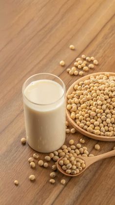 a wooden spoon with some soy seeds next to a glass of milk