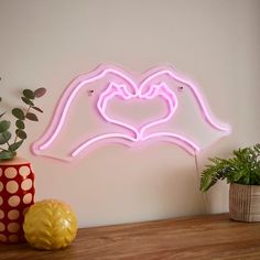 a pink neon sign with two hands holding a heart