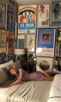 a woman laying on top of a bed in a room filled with pictures and posters