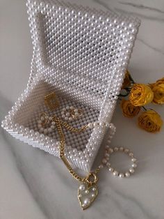 a white beaded box with pearls and gold jewelry in it next to yellow roses