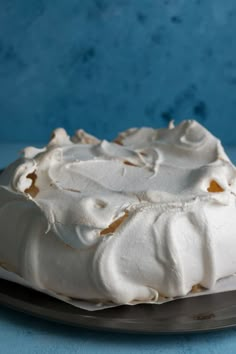 a cake with white frosting sitting on top of a metal plate next to a blue wall