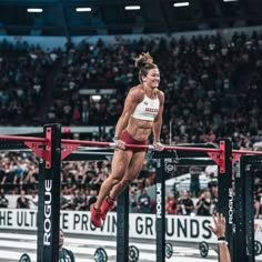 a woman is jumping over a bar in a crossfit competition at the stadium