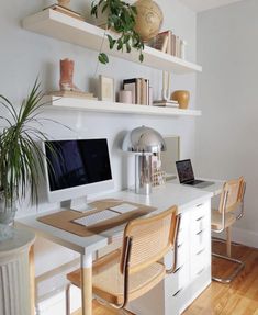 a desk with a computer on top of it next to two chairs and a potted plant