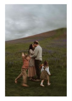 two adults and three children walking in a field with purple flowers on the hill behind them