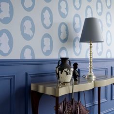 a table with a lamp and vase on it next to a wallpapered background