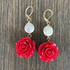 two red roses are hanging from gold earwires on a wooden table with beads