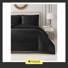 a bed with black sheets and pillows in a white room next to a gold mirror