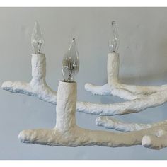 three light bulbs are placed on the base of a tree branch chandelier that is made out of clay