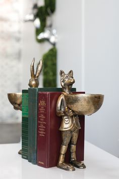 a bookend with a gold rabbit holding a bowl on it's back and two books in the background