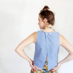 a woman standing in front of a white wall wearing a blue shirt and floral skirt