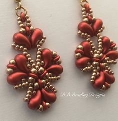 two red and gold earrings with beads on them, one is dangling from a chain