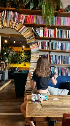 a woman sitting at a table in front of a bookshelf filled with books